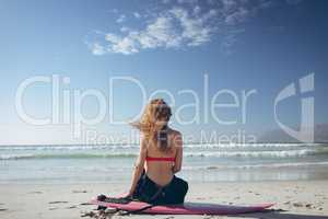 Female surfer sitting on surfboard at beach