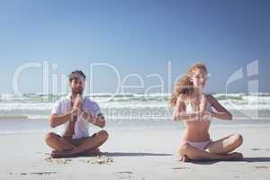 Couple sitting in lotus positions and practicing yoga on beach