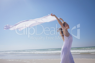 Beautiful woman holding scarf on beach