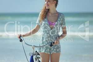 Happy woman holding bicycle at beach on a sunny day