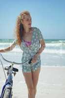 Happy woman holding bicycle at beach on a sunny day
