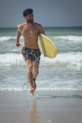 Young male surfer with a surfboard running at beach