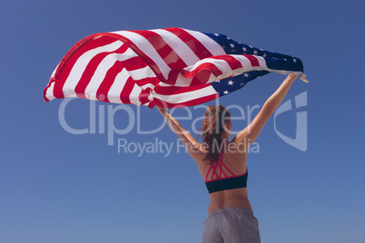 Young woman holding american flag at beach on sunny day