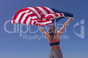 Young woman holding american flag at beach on sunny day