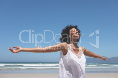Beautiful woman standing with open arm at beach on sunny day