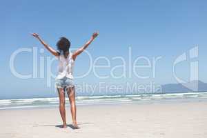 Beautiful woman standing with open arm at beach on sunny day
