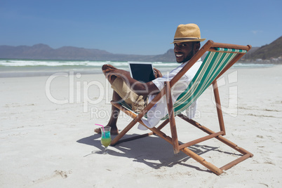 Young man using laptop while sitting on sun lounger at beach