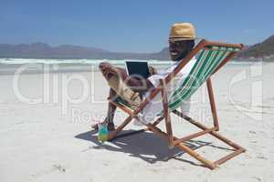 Young man using laptop while sitting on sun lounger at beach