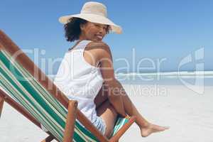 Young woman giving pose while sitting on sun lounger at beach