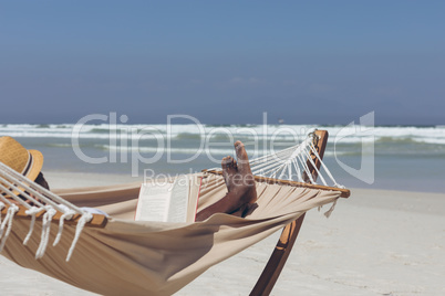 Man reading book while relaxing on hammock at beach