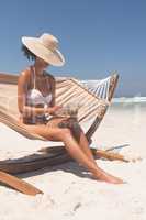 Woman using digital tablet while sitting on hammock at beach