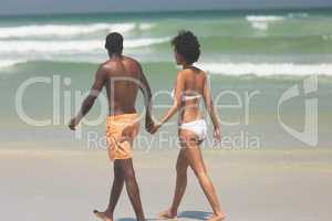 Couple holding hands and walking at beach on a sunny day