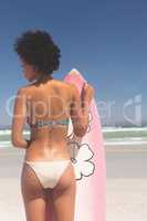 Female surfer with a surfboard standing on a beach