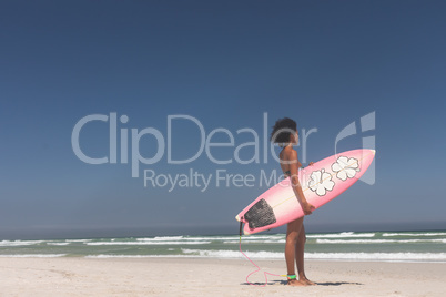 Female surfer with a surfboard standing on a beach