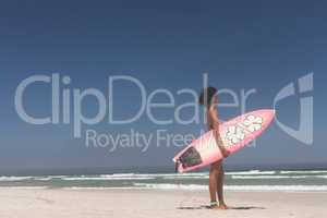 Female surfer with a surfboard standing on a beach