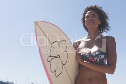 Female surfer with a surfboard standing on a beach