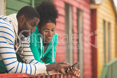 Couple using mobile phone while standing near beach hut