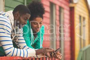 Couple using mobile phone while standing near beach hut
