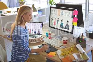 Female fashion designer using graphic tablet while working at desk