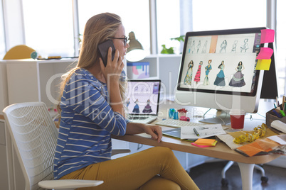 Female fashion designer talking on mobile phone while working at desk