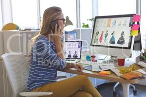 Female fashion designer talking on mobile phone while working at desk