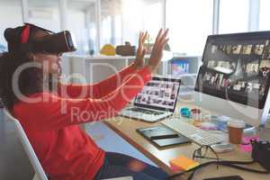 Female graphic designer using virtual reality headset at desk