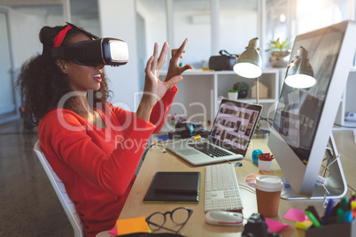 Female graphic designer using virtual reality headset at desk