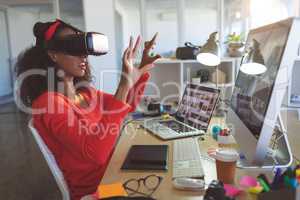 Female graphic designer using virtual reality headset at desk