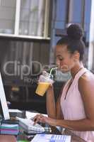 Businesswoman having milkshake while working on computer at desk