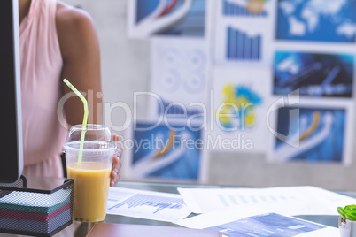 Businesswoman holding milkshake glass while working on computer at desk in the office