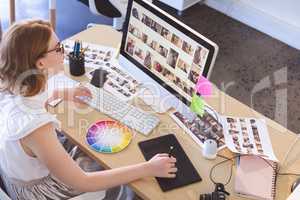 Female graphic designer working on graphic tablet and computer at desk in office