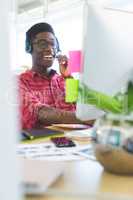 Graphic designer talking on headphone while working at desk in office