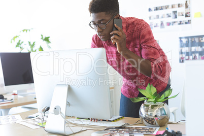 Graphic designer talking on mobile phone while working on computer at desk