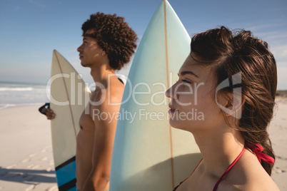 Thoughtful young couple standing with surfboards on the beach
