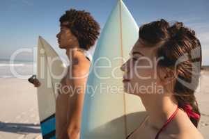 Thoughtful young couple standing with surfboards on the beach