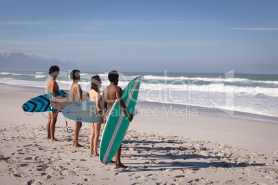 Group of friends with surfboard standing at beach in the sunshine