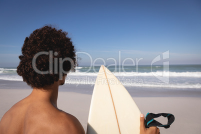 Young man standing with surfboard at beach in the sunshine