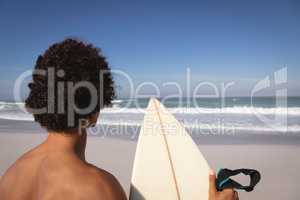 Young man standing with surfboard at beach in the sunshine