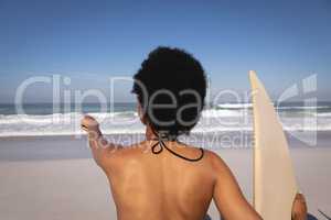 Young woman with surfboard pointing at sea on beach in the sunshine