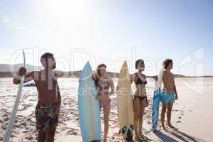 Group of friends with surfboard standing at beach in the sunshine