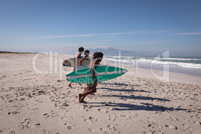 Group of friends with surfboard running towards sea at beach in the sunshine