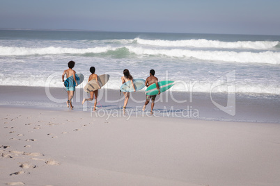 Group of friends with surfboard running towards sea at beach in the sunshine