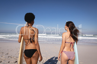 Young women with surfboard standing at beach in the sunshine