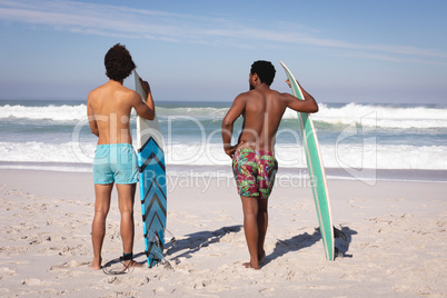Young men with surfboard standing at beach in the sunshine