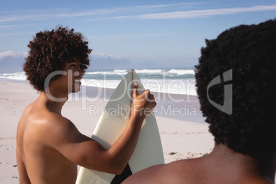 Young men with surfboard standing at beach in the sunshine