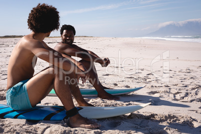 Young men interacting with each other while sitting on surfboard at beach