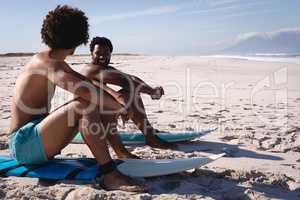 Young men interacting with each other while sitting on surfboard at beach