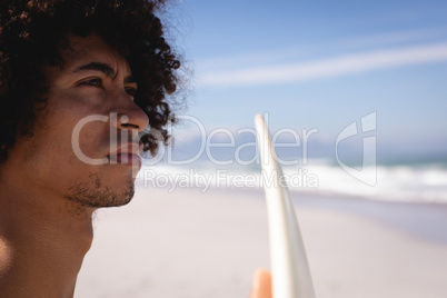 Thoughtful young man with surfboard standing on the beach