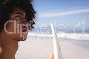 Thoughtful young man with surfboard standing on the beach