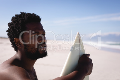 Thoughtful young man with surfboard standing on the beach